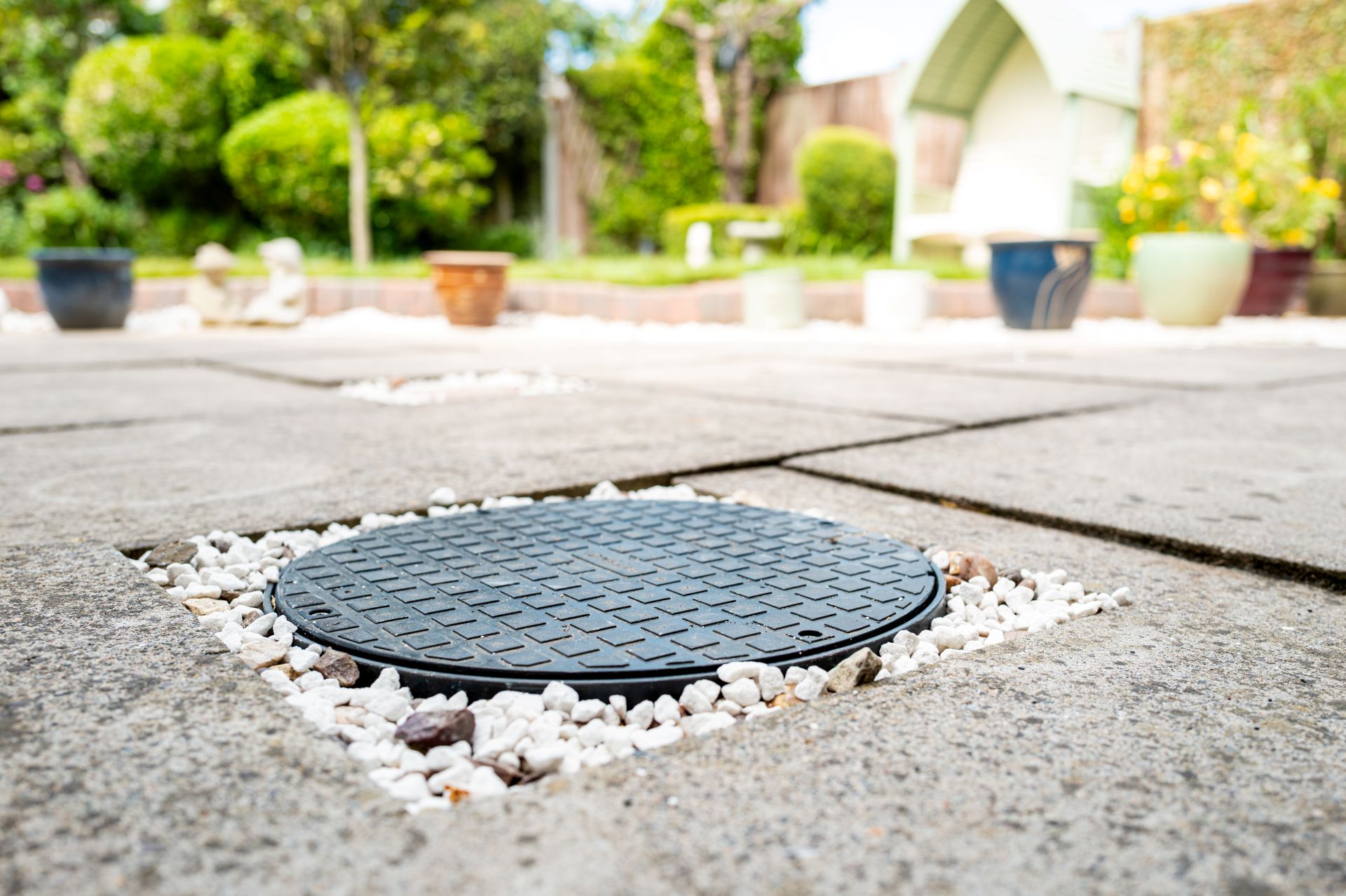 Flache Tankabdeckung einer unterirdischen Regenwassernutzungsanlage in gepflasterter Gartenfläche